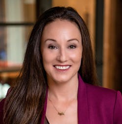 The image features a woman with long dark hair, smiling and dressed in a burgundy blazer, in a professional setting.