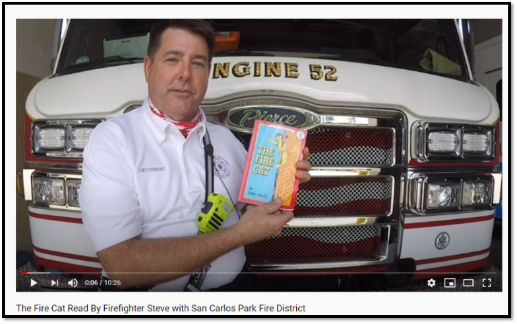 A firefighter holds "The Fire Cat" book in front of fire engine 52.