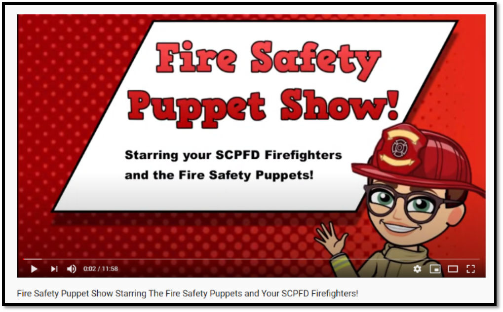 Fire Safety Puppet Show featuring SCPFD Firefighters and Fire Safety Puppets. Cartoon character waves in a firefighter hat.