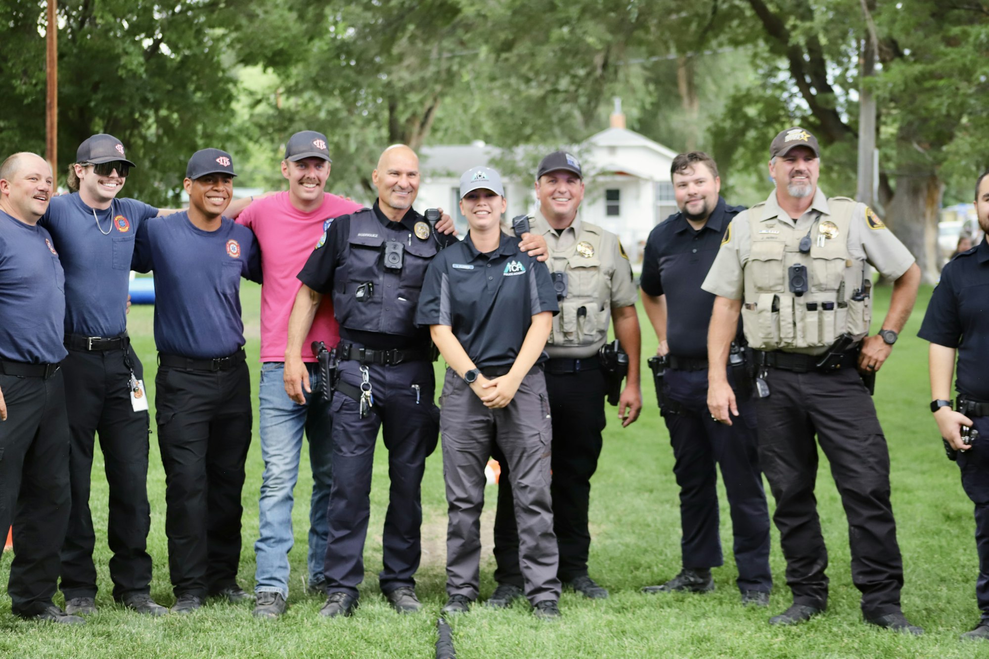 Group of smiling law enforcement officers and firefighters posing together outdoors.