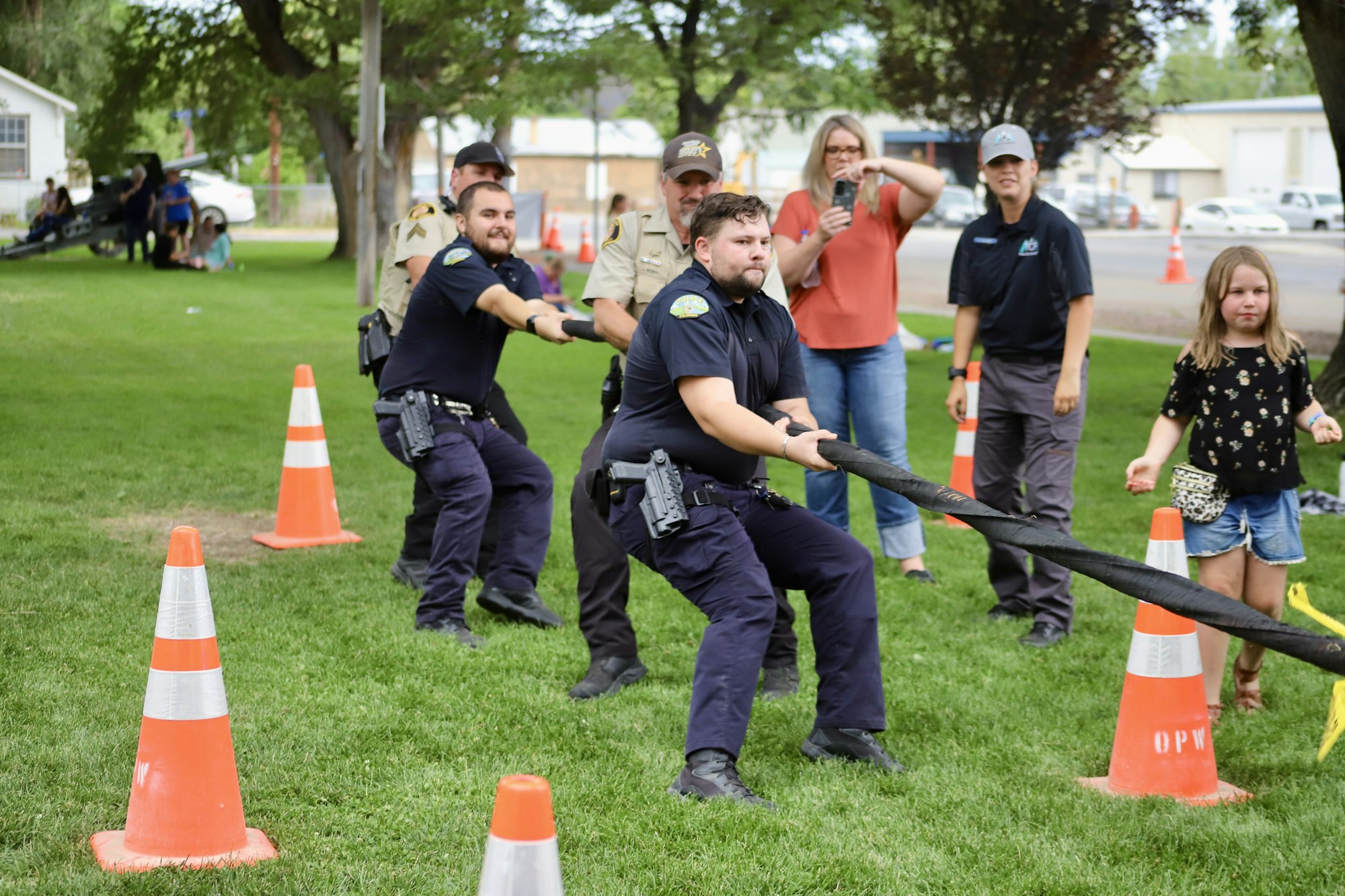 A group of police officers engaged in a tug-of-war game on a grassy field, with onlookers cheering them on.