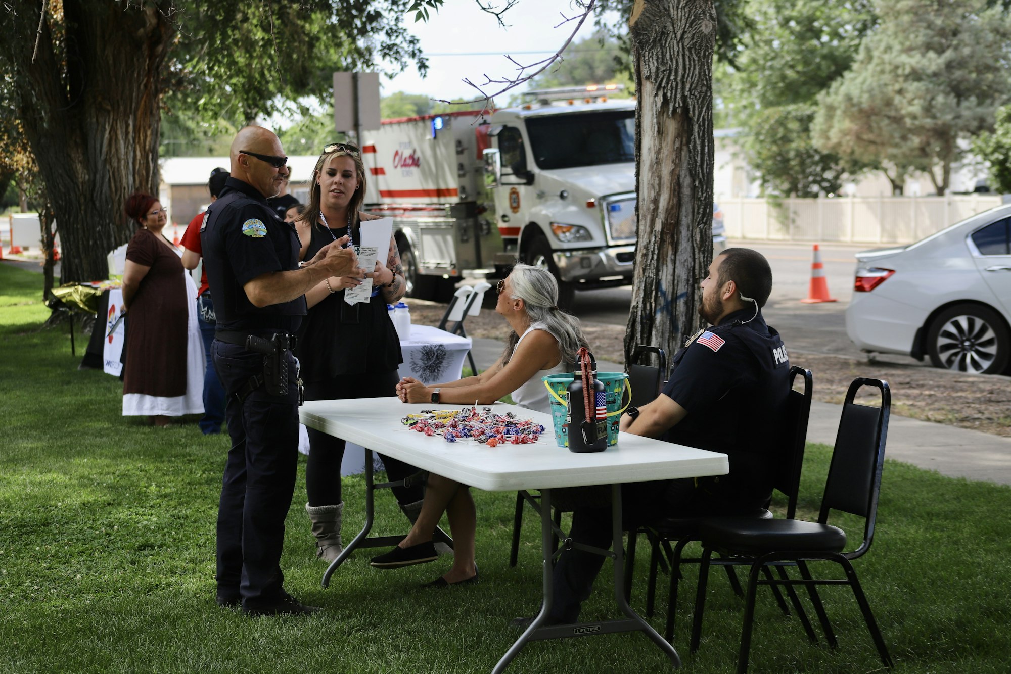 This image shows people gathered, including police officers, around a table with candy, likely at an outdoor community event.