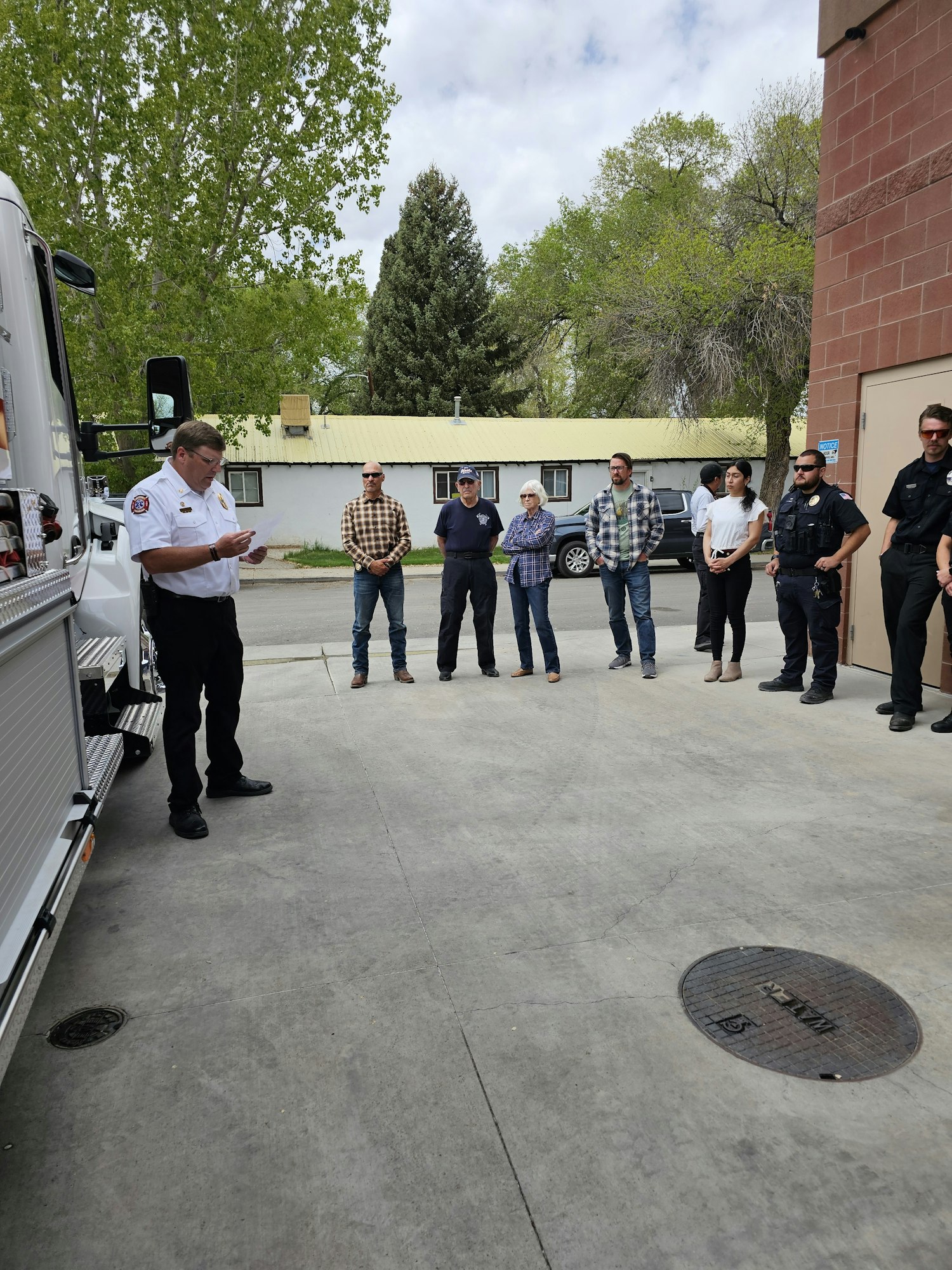 A group of people outside, with one in uniform, possibly a firefighter or officer, speaking or presenting. Image is rotated.