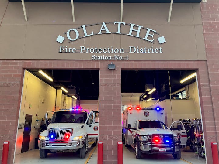 A firetruck and an ambulance at "Olathe Fire Protection District Station No.1" with lights on.
