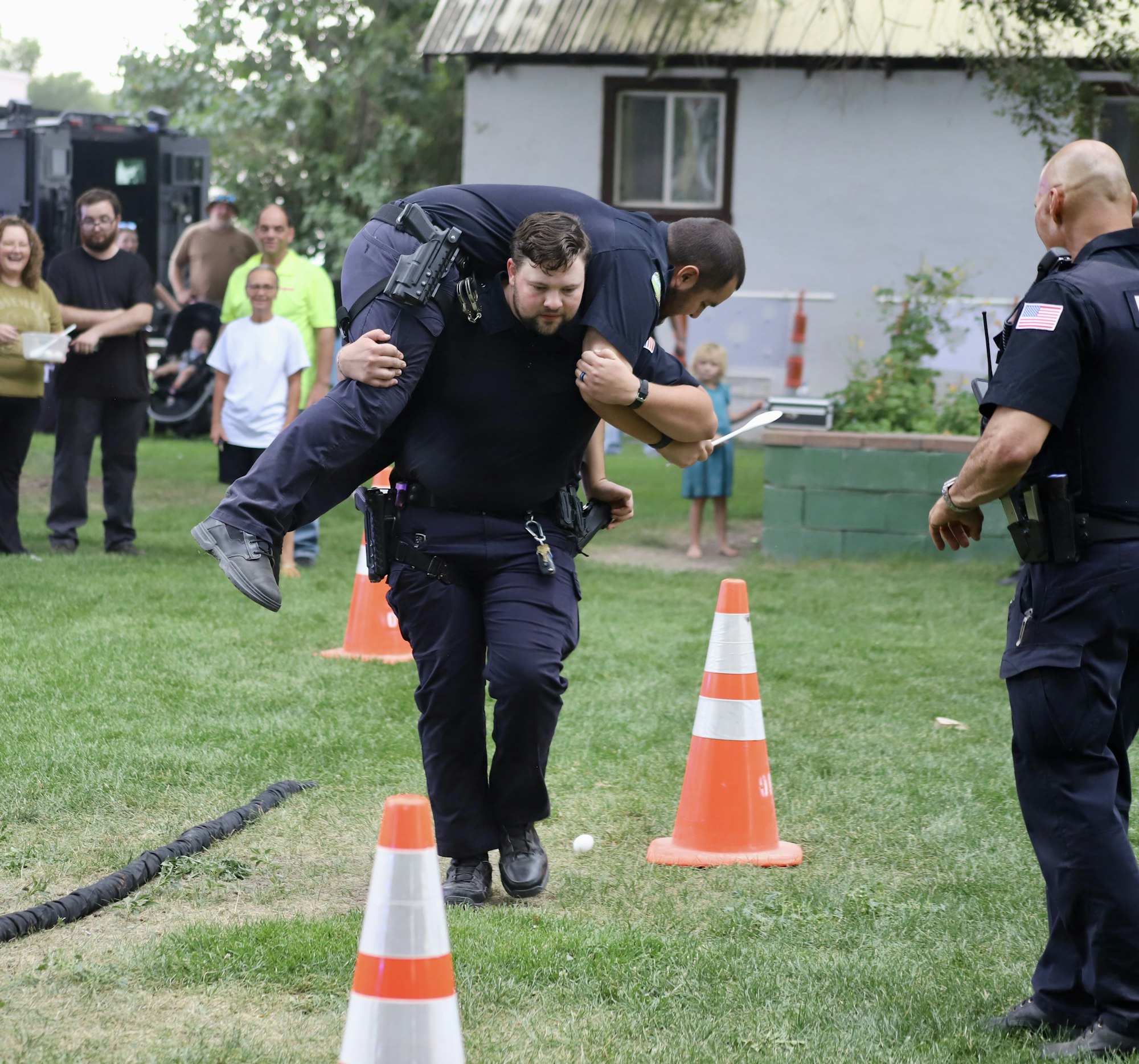 A police officer is carrying another officer on his back during an outdoor event with spectators.