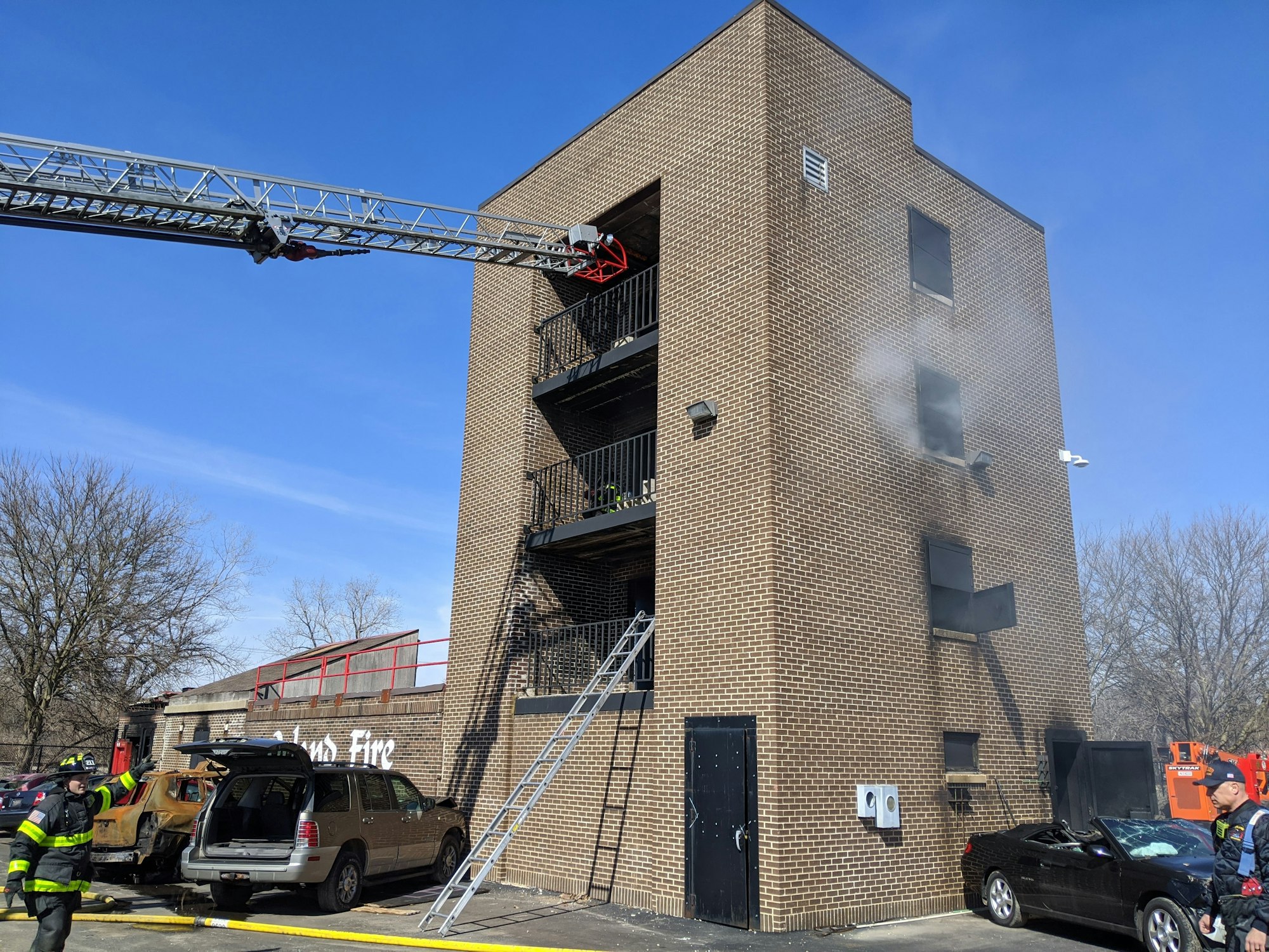 Firefighters responding to a smoke-filled building with ladder truck extended.