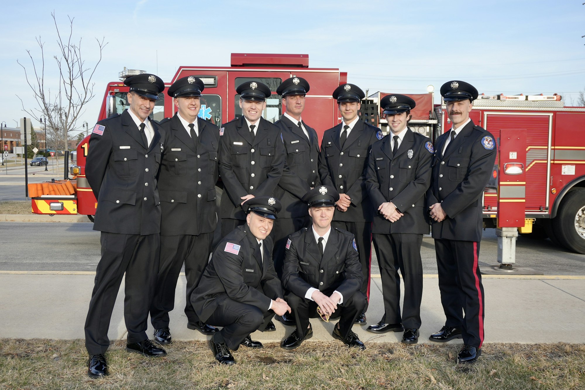 A group of uniformed firefighters is posing in front of a red fire truck.