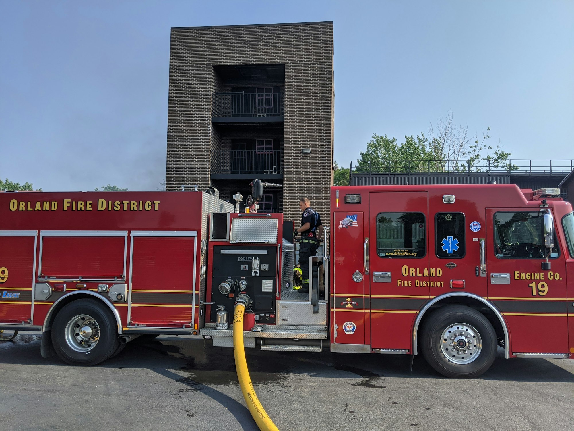 A fire engine and firefighter at a building with visible smoke.