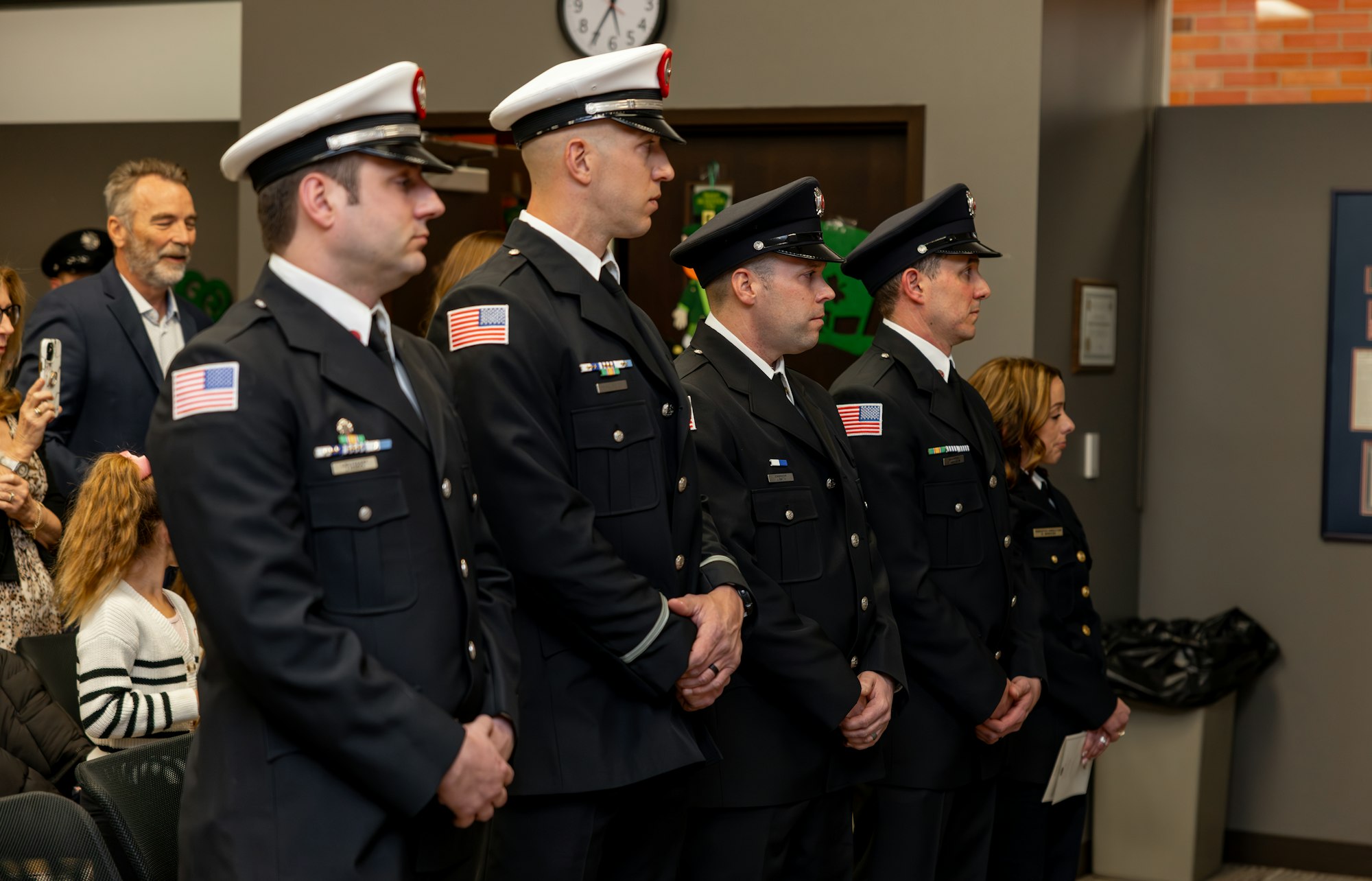 A line of uniformed personnel stands at attention, with onlookers in the background, suggesting a formal event or ceremony.