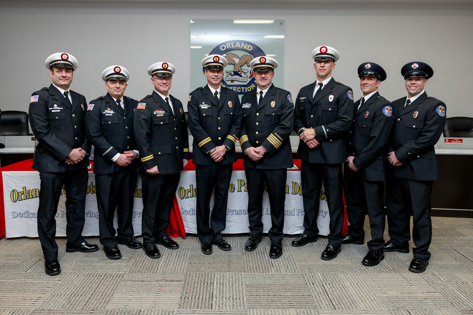 A group of uniformed officials, likely firefighters or police, posing in front of a banner for the Orlando Protection District.