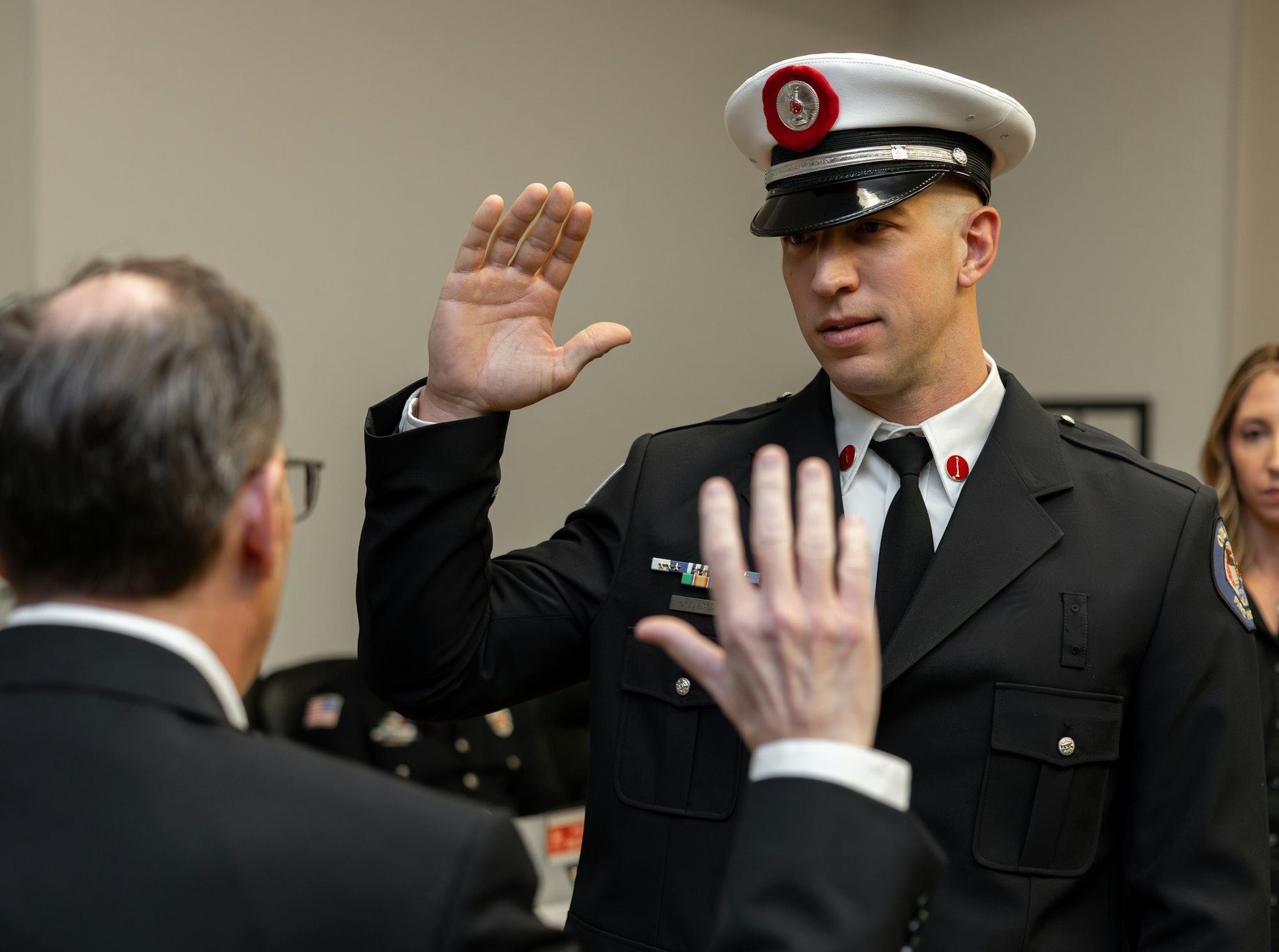 A uniformed individual is taking an oath during a ceremony, raising their hand, while a second person gestures in front of them.
