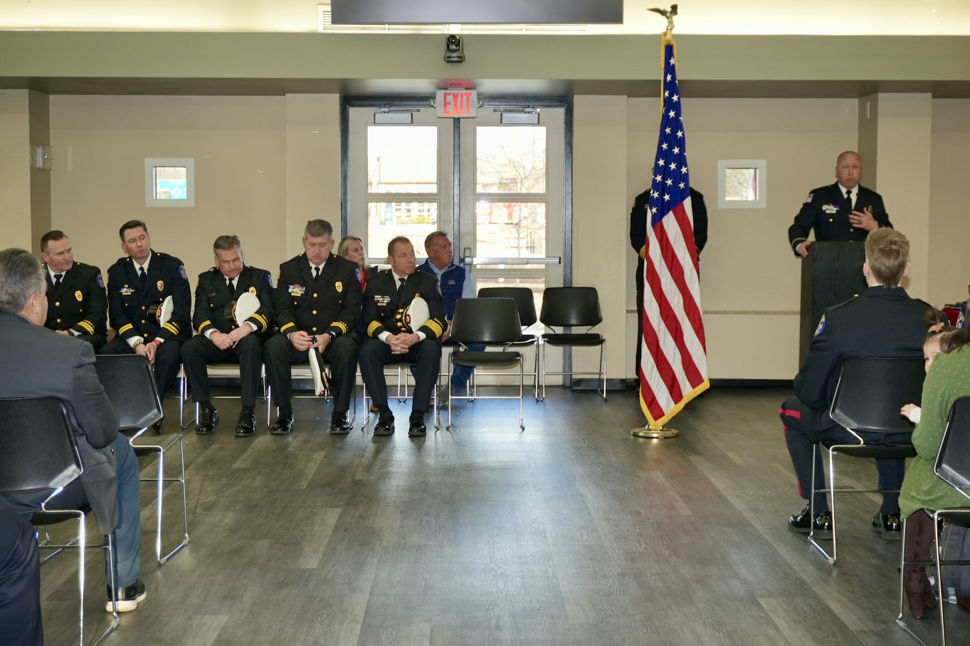 A speaker at a podium addresses uniformed officials seated beside an American flag.