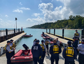People in life jackets by a dock with boats, likely a water rescue training or briefing.