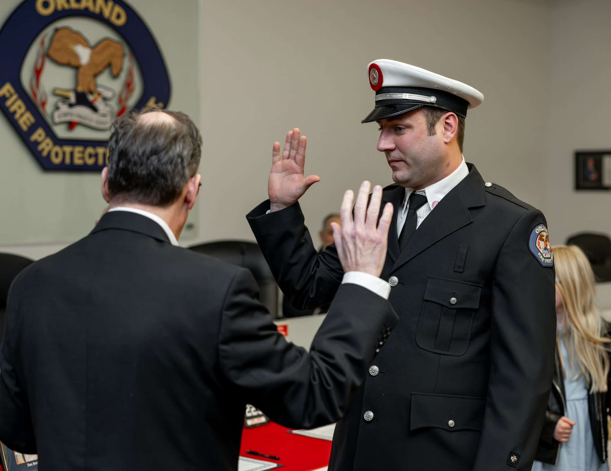 A firefighter is taking an oath in a formal ceremony, with a badge and supportive attendees present.