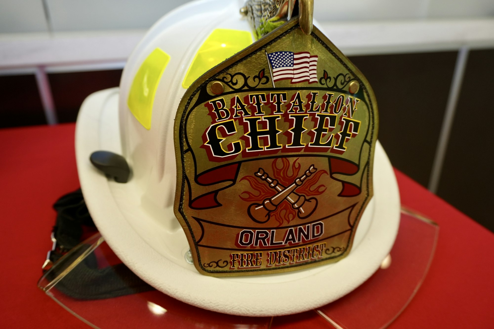 A firefighter's helmet with a "Battalion Chief, Orland Fire District" badge and an American flag design.