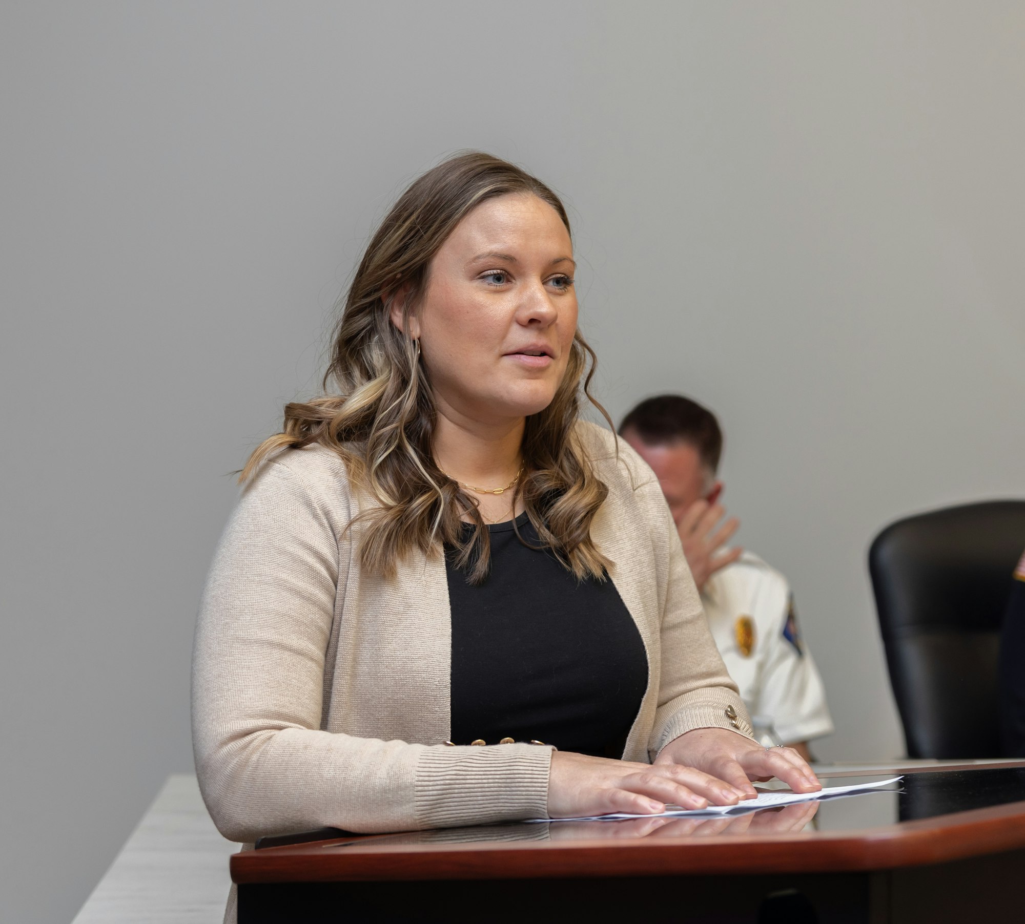 A woman speaks at a table in a meeting room, with a focus on her expression and engagement. Other individuals are present.