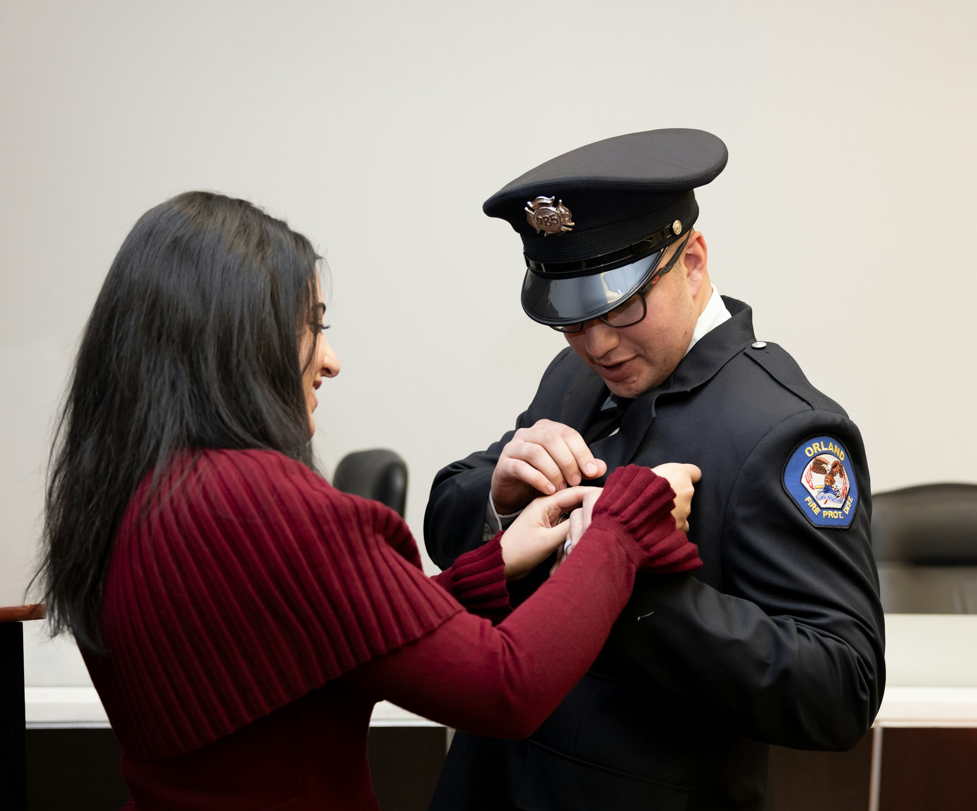 A woman is pinning a badge on a new firefighter's uniform during a ceremony.