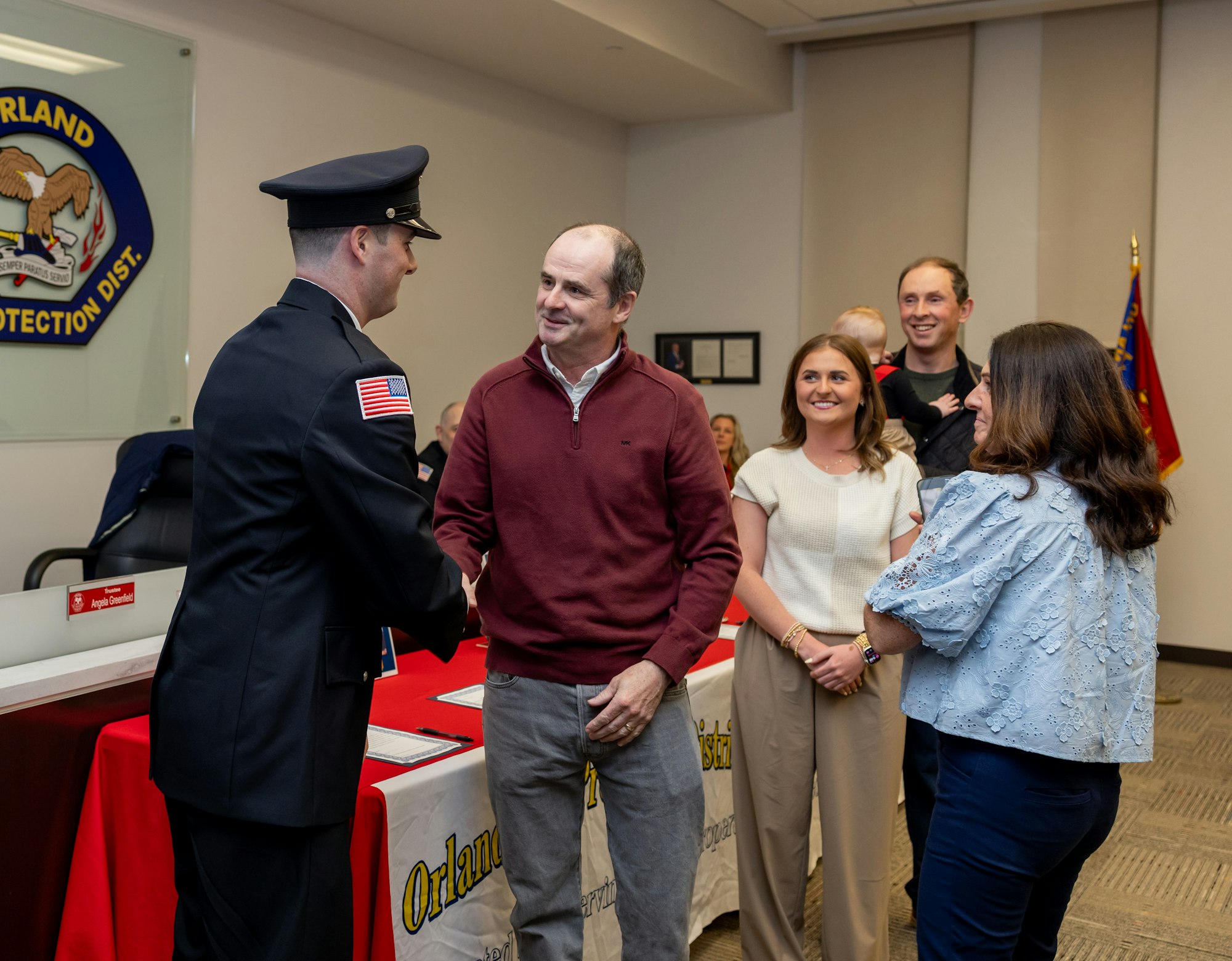 A ceremony where a person in uniform shakes hands with a man, surrounded by family and friends, celebrating an achievement.