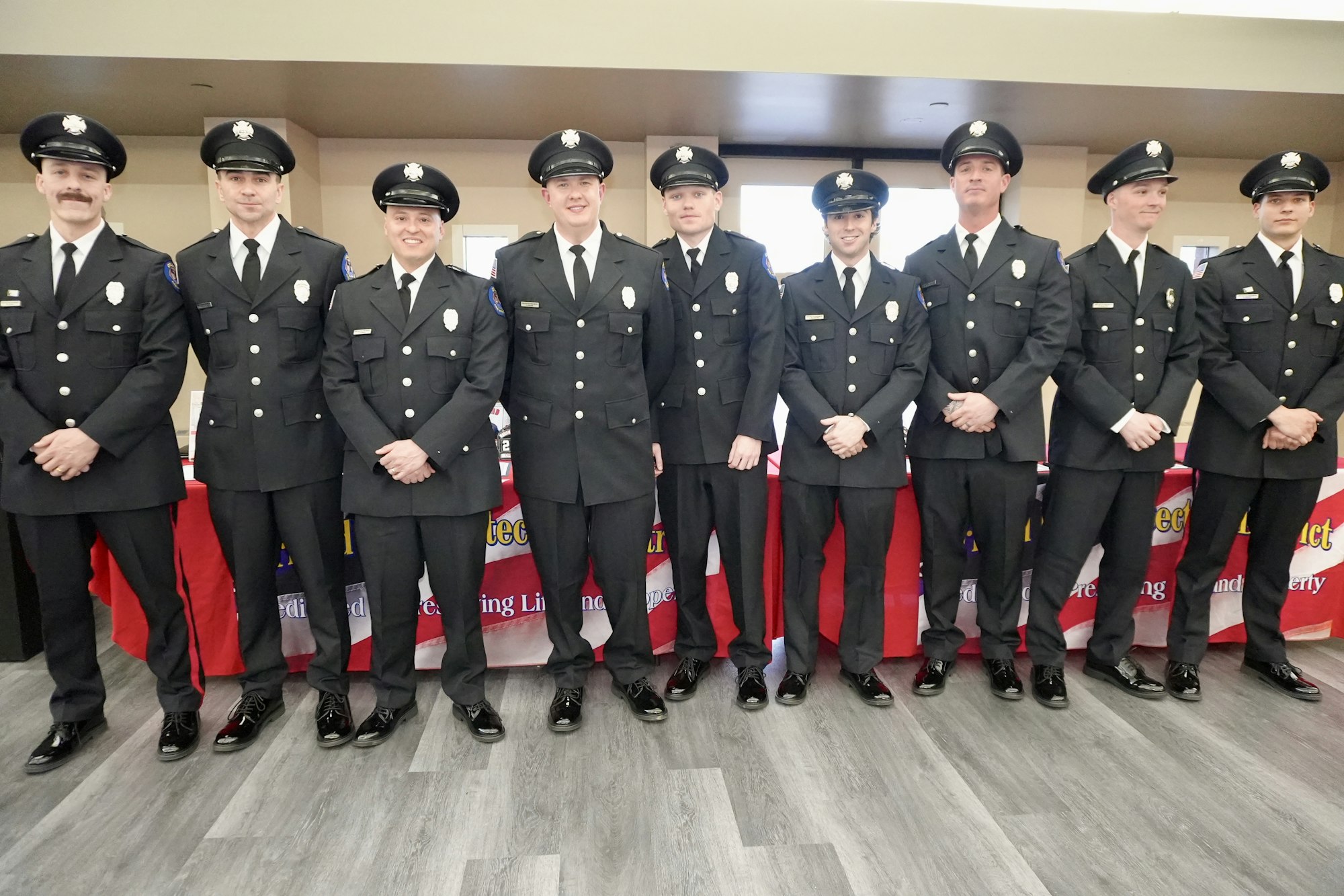 A group of uniformed individuals stands together indoors, smiling.
