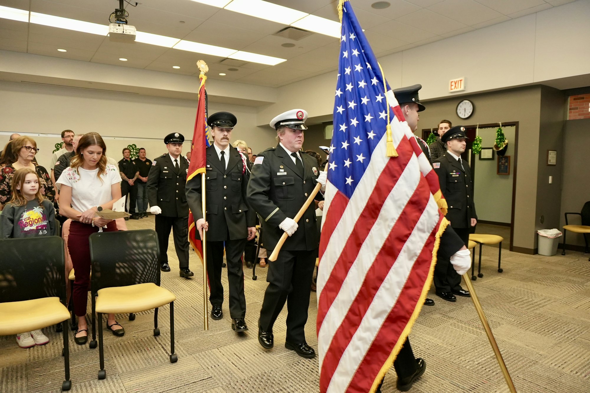 Uniformed officers carrying flags in a room with people seated and standing.