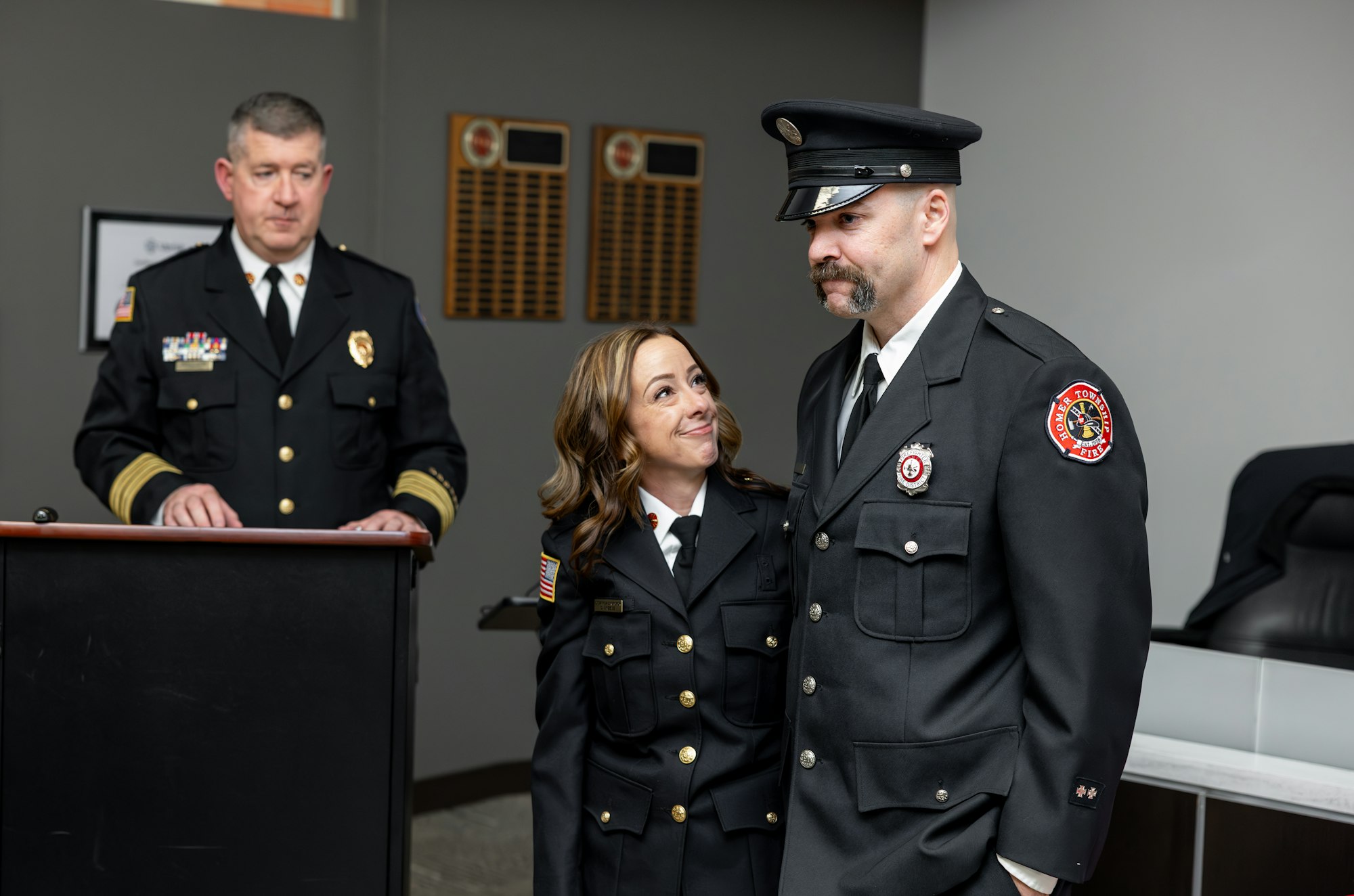 A ceremony featuring a uniformed officer speaking, with two others, one appearing happy, standing nearby, likely celebrating an achievement.