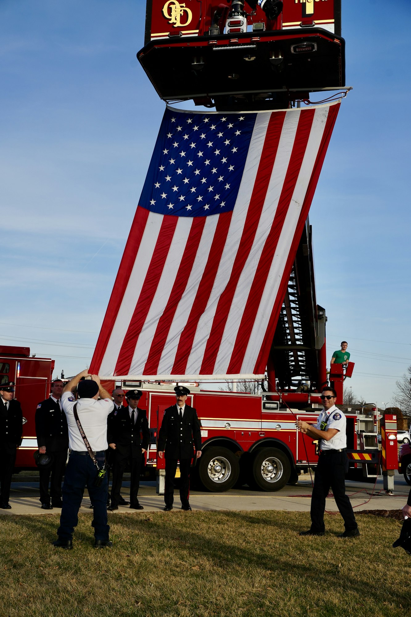 Firefighters stand by a large American flag hanging from a fire truck ladder.