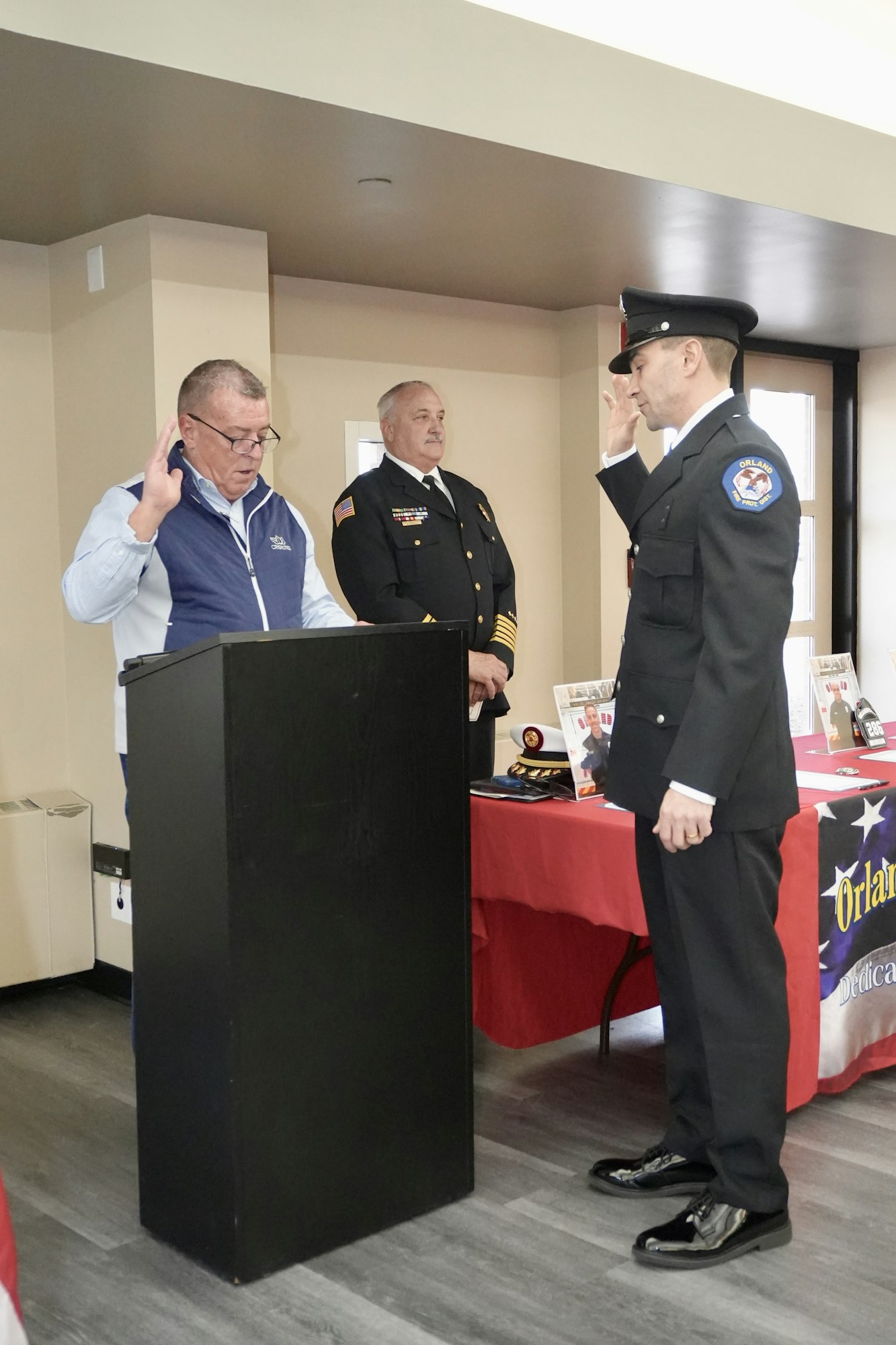 A firefighter ceremony with a man being sworn in, raising his right hand, and two others present.