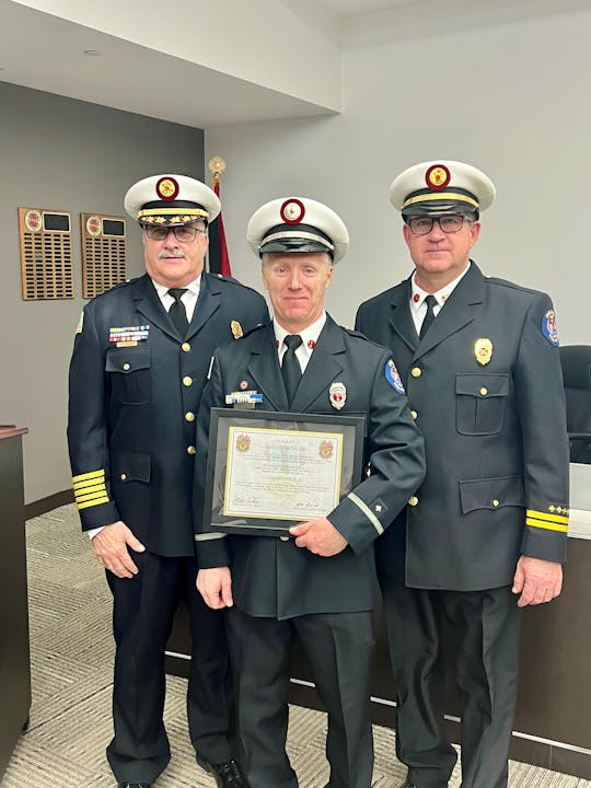 Three men in uniform, with hats, posing for a photo. One holds a framed certificate.
