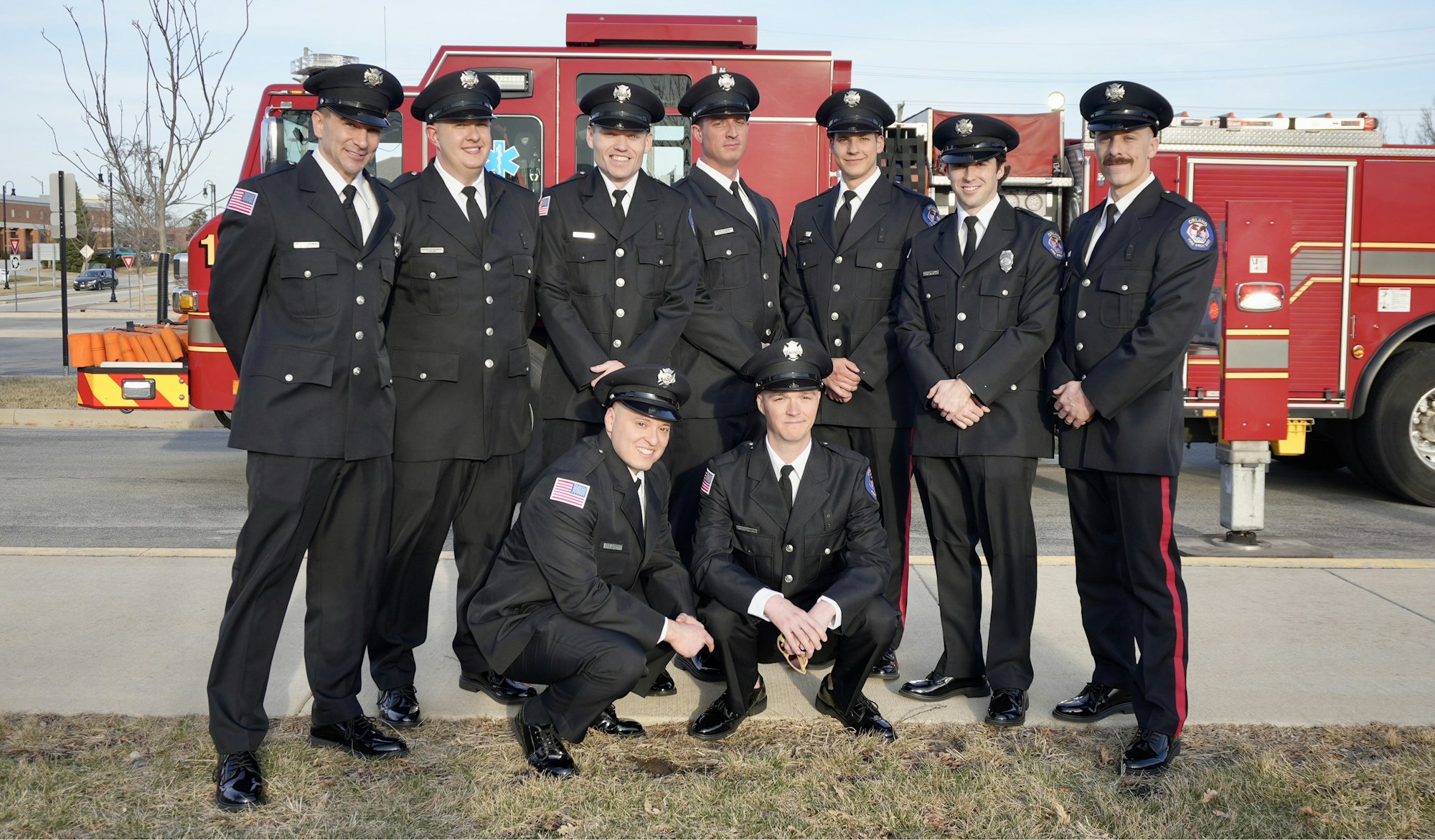 A group of uniformed firefighters posing in front of a fire truck.
