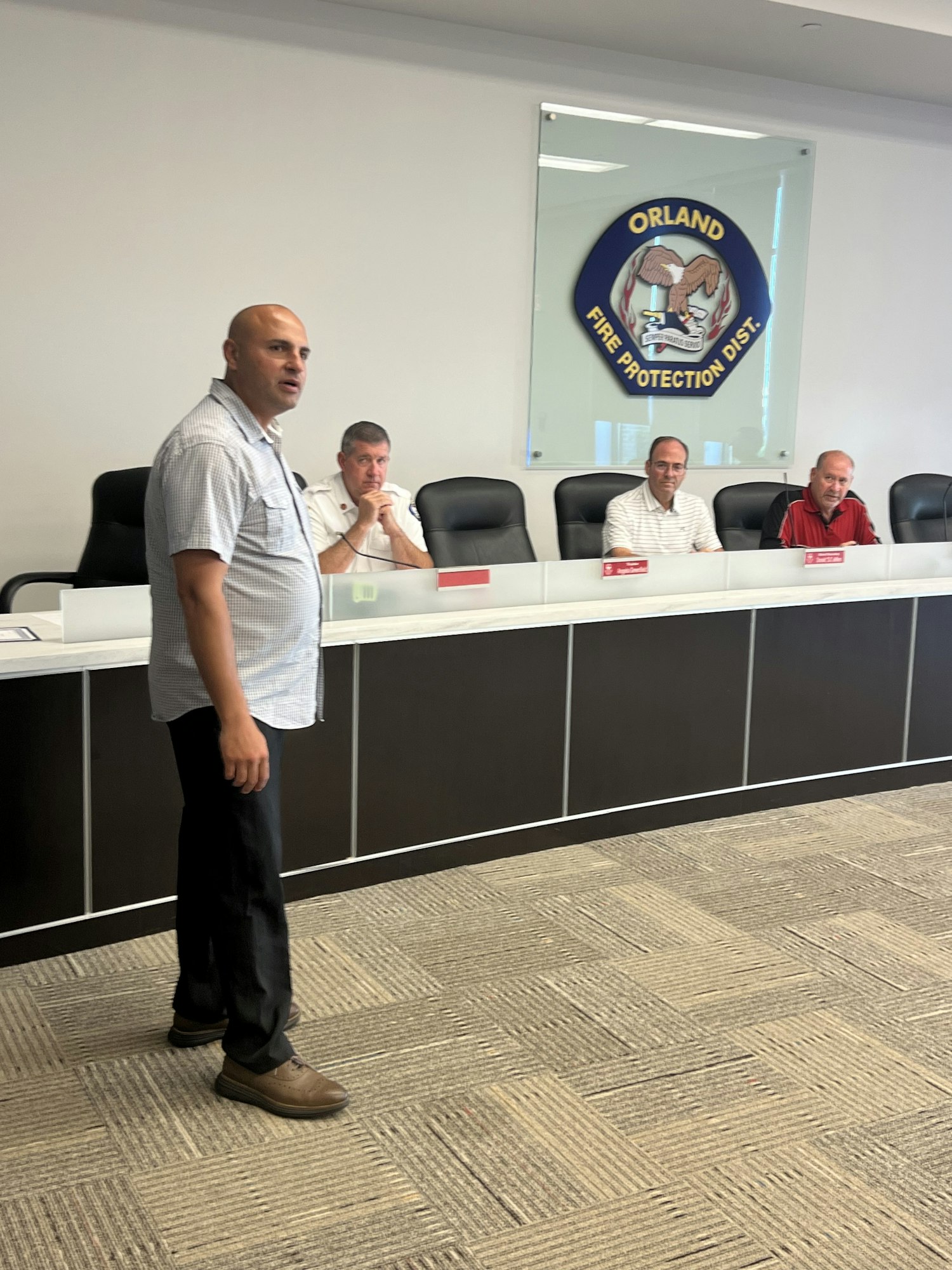 Four people in a meeting room with the Orland Fire Protection District emblem on the wall.