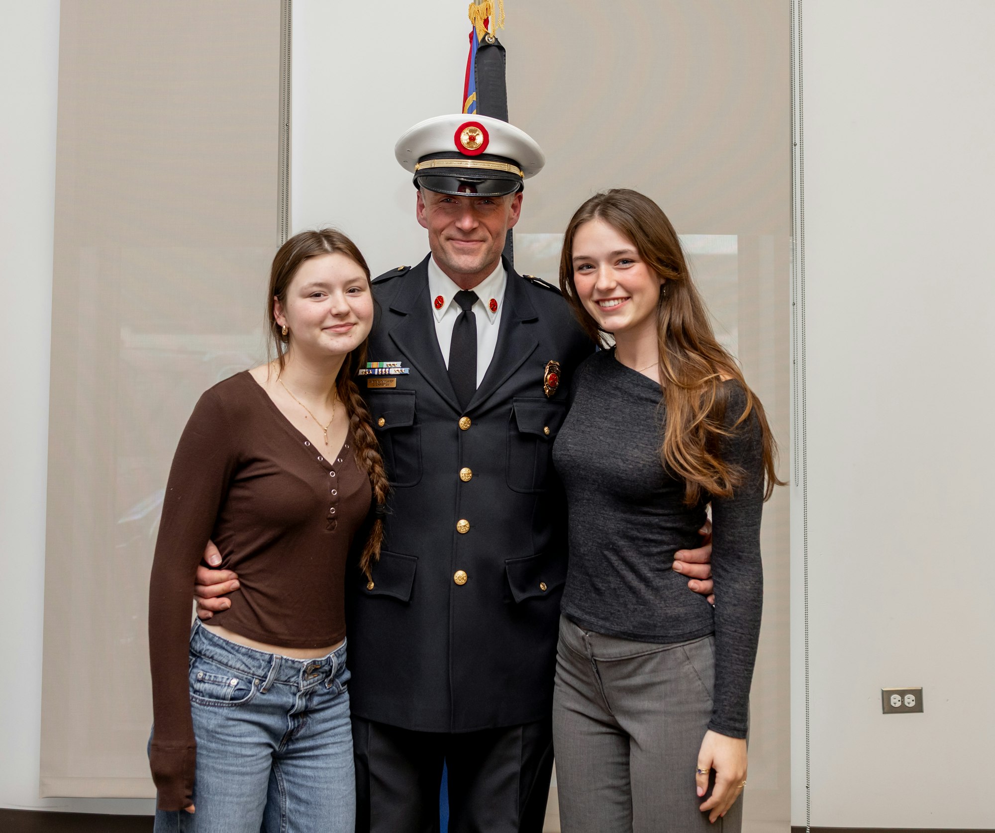 A man in uniform poses with two young women, smiling for a photo.