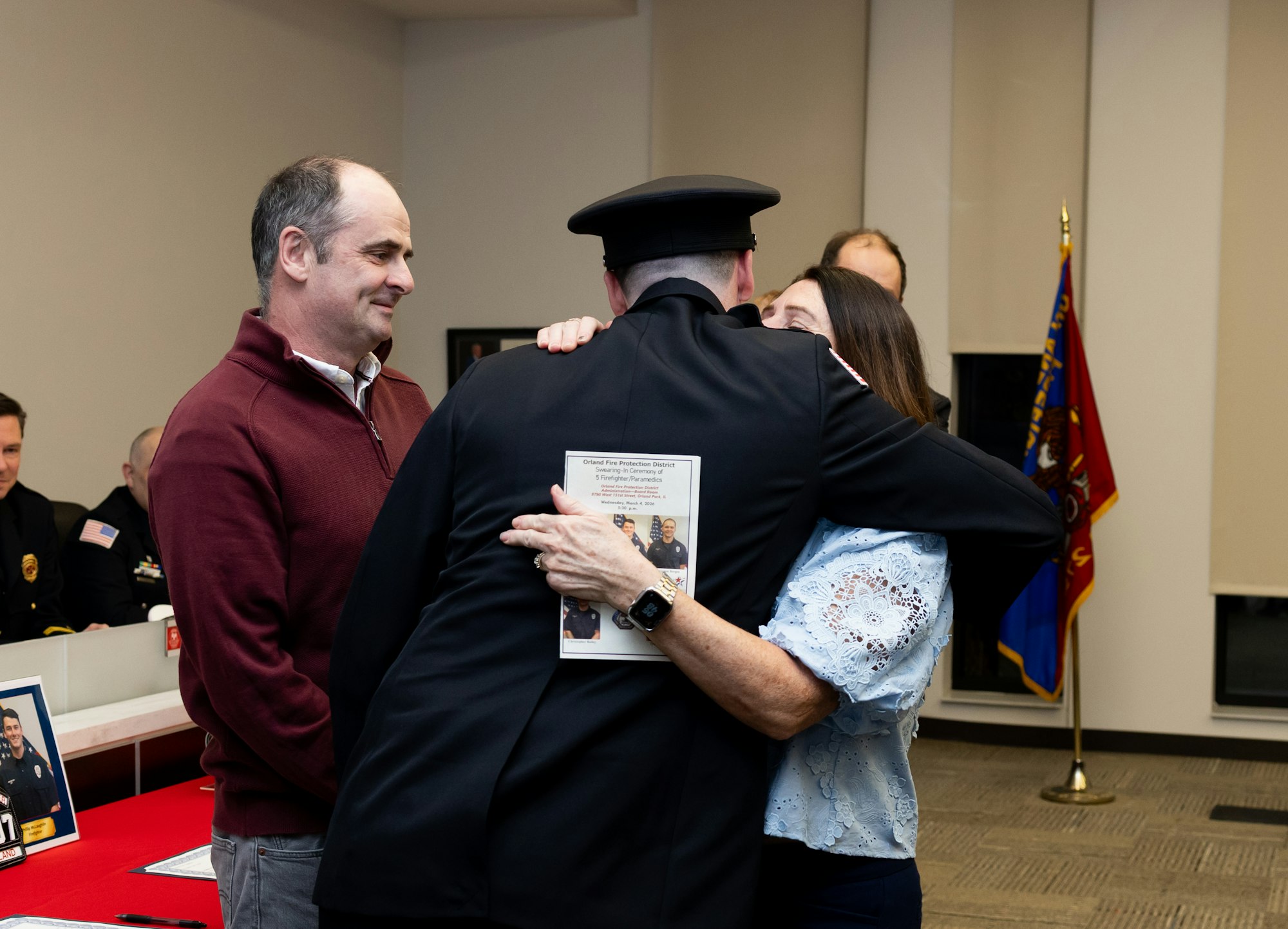 A heartfelt moment with a firefighter hugging a woman, while a man looks on, possibly during a ceremony or celebration.