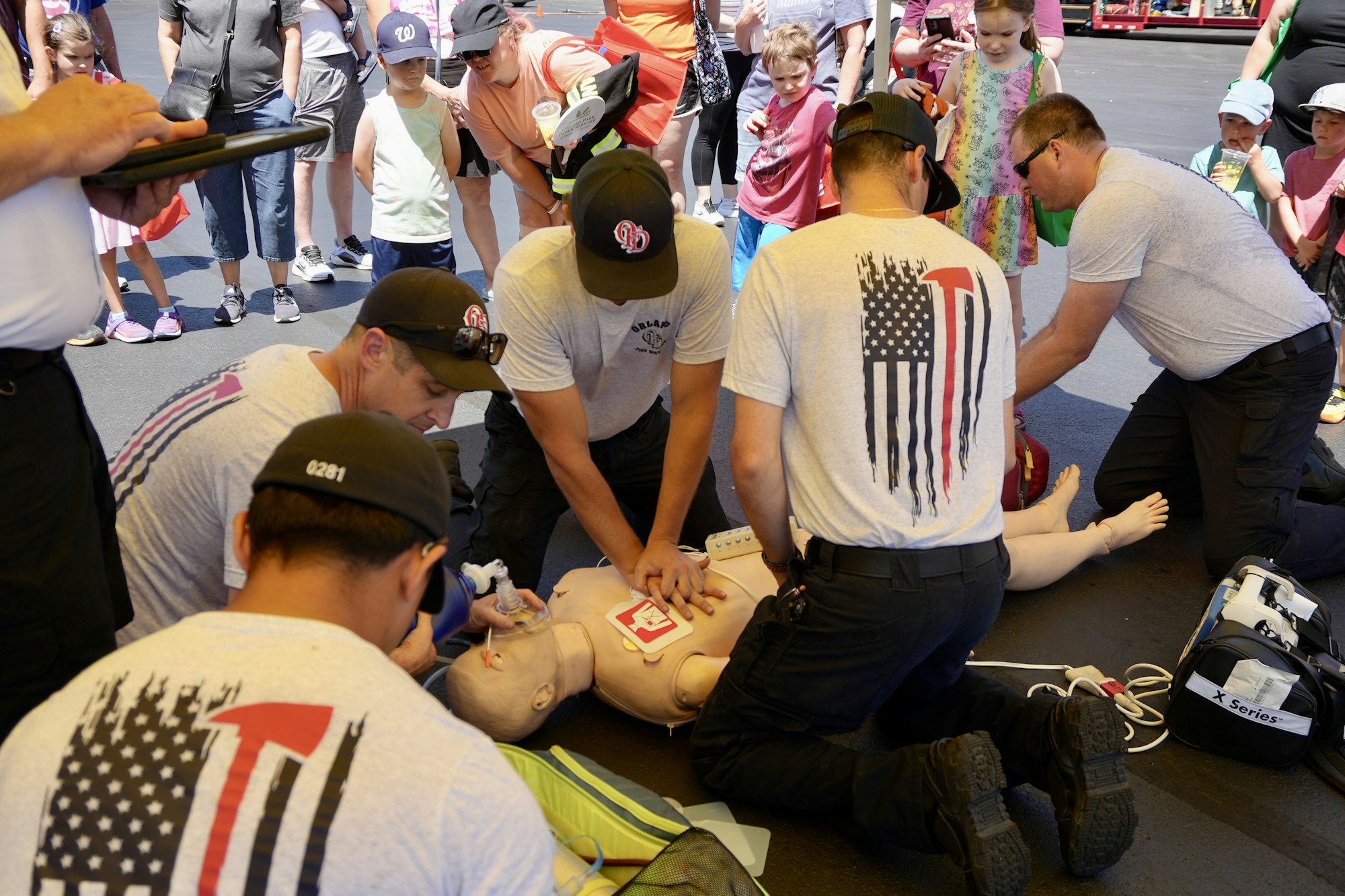 People demonstrating CPR on a mannequin while a group watches attentively.