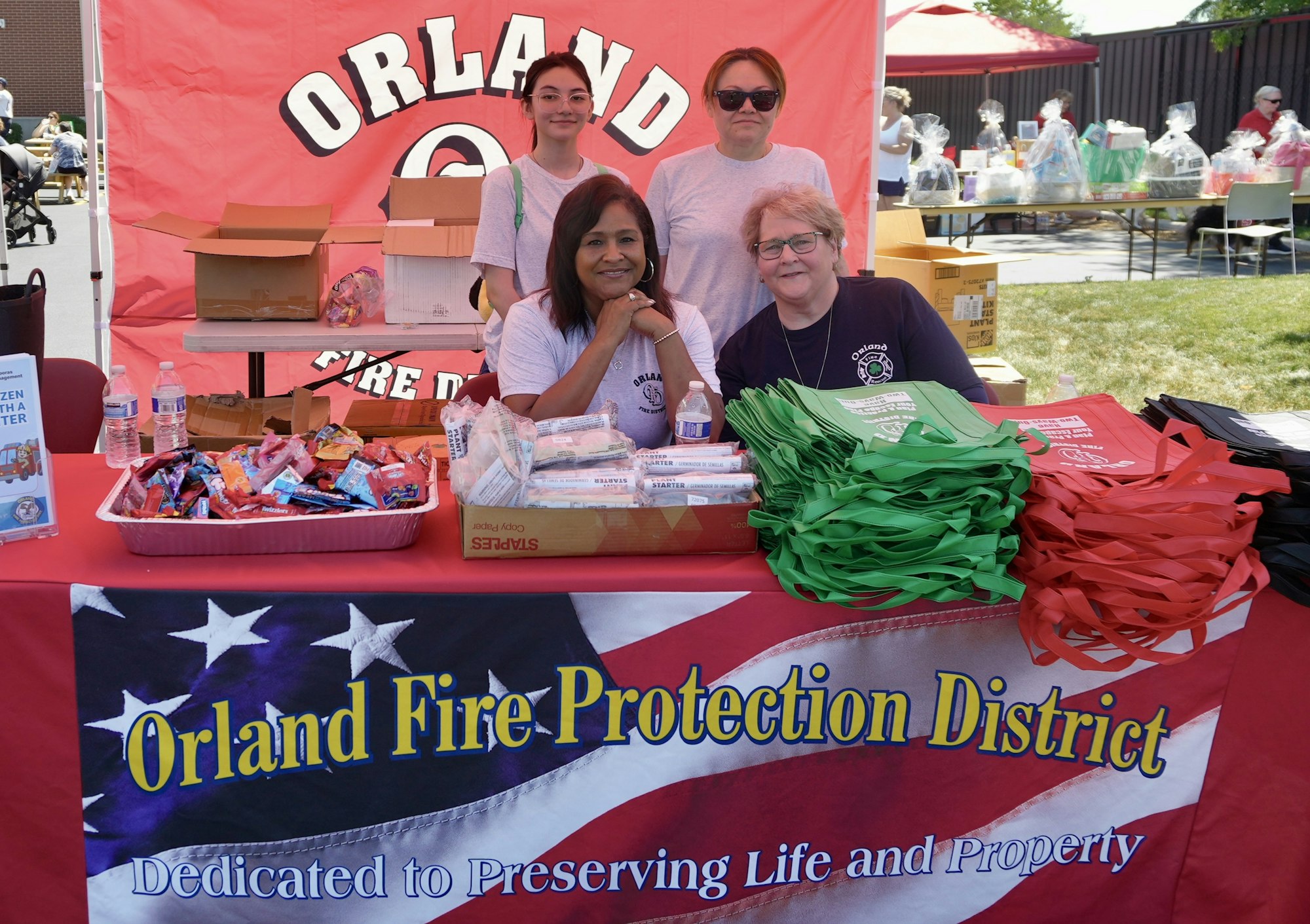 Four people at an Orland Fire Protection District booth with snacks and bags, promoting fire safety.
