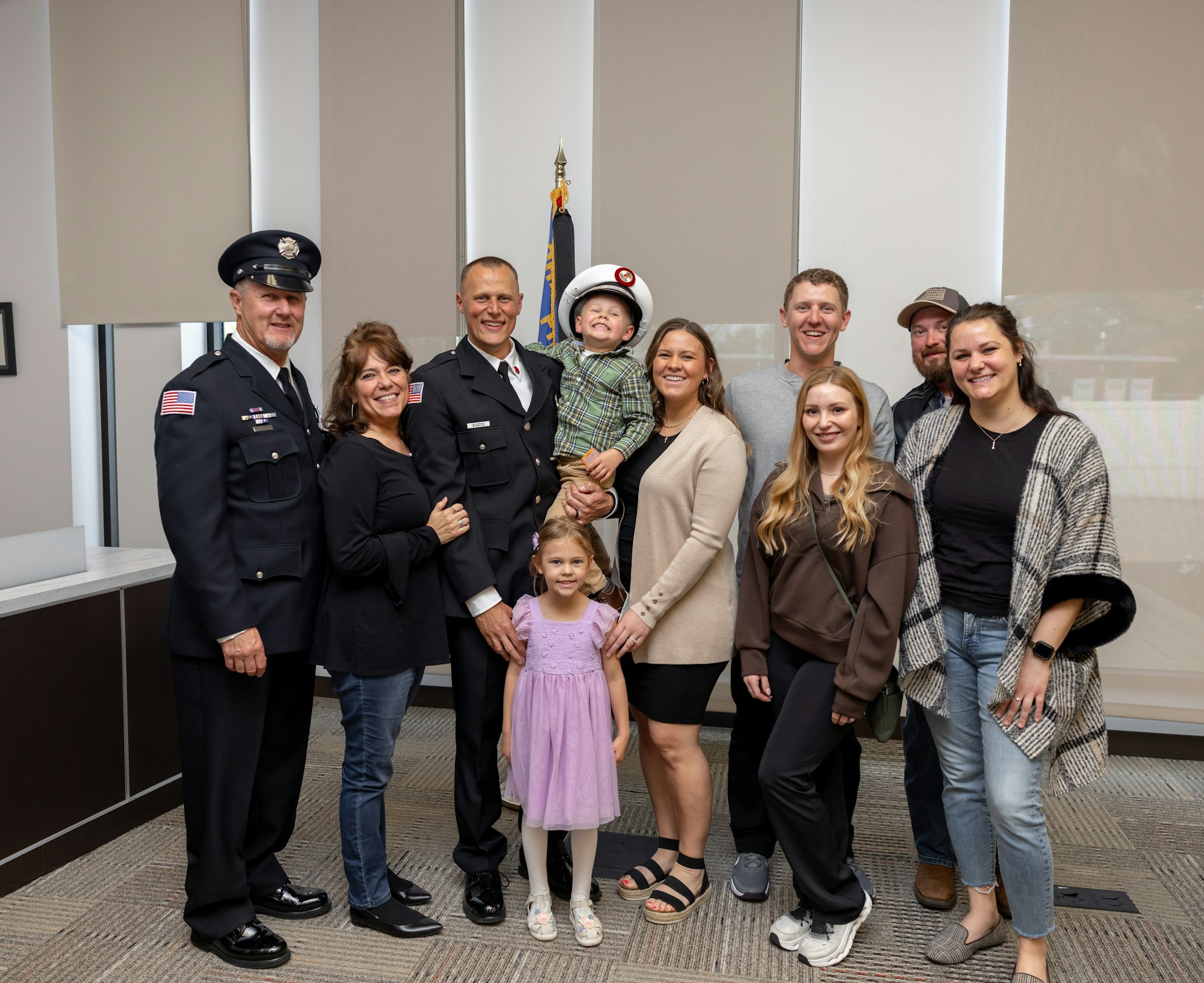 A group photo featuring firefighters in uniform with family members, including children, celebrating a special occasion.