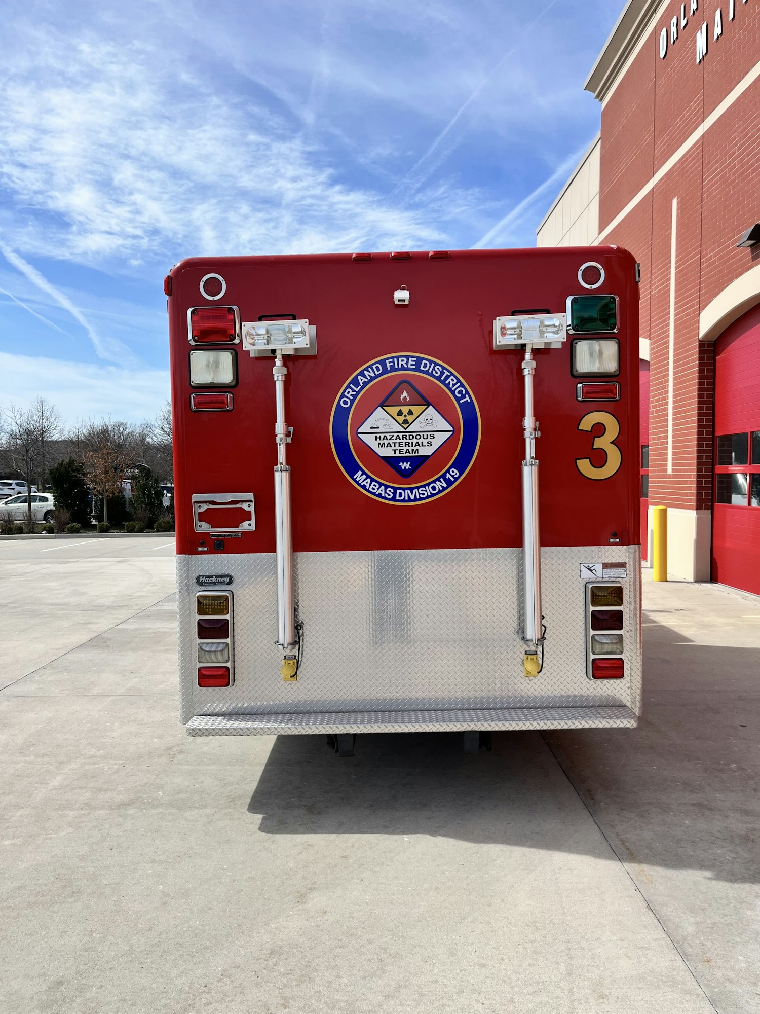 The image shows the back of a red ambulance with emergency lights, a district emblem, and the number 3.
