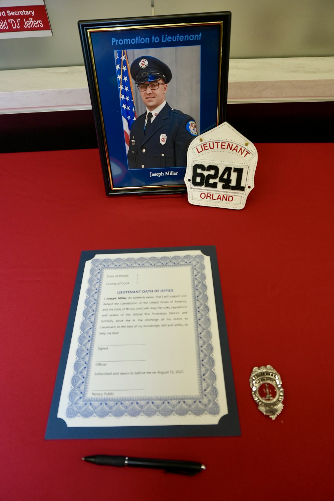 Promotion to Lieutenant display with photo, badge, plaque, oath, and pen on a red table.