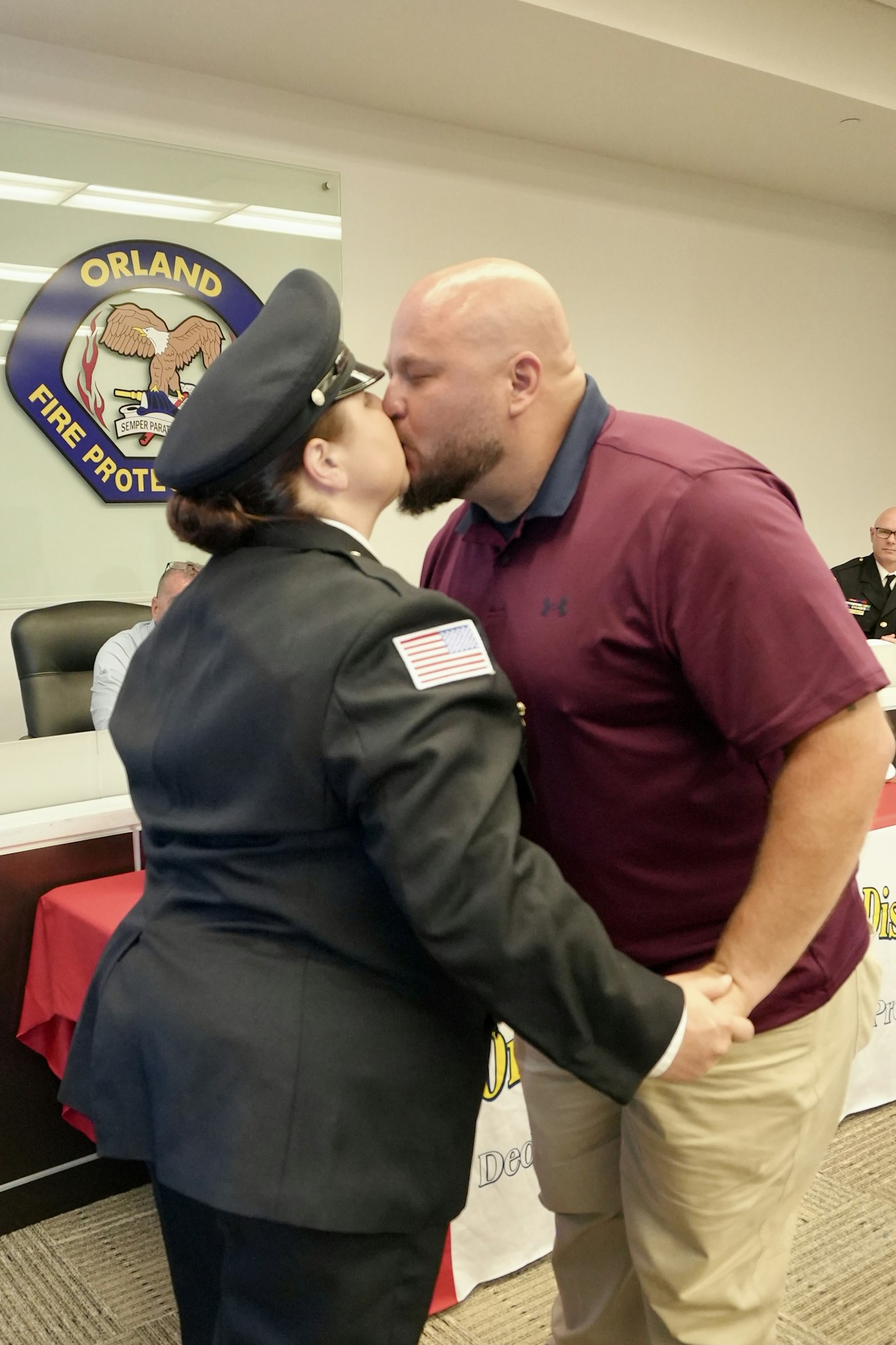 A person in a fire department uniform and a man are kissing, holding hands in a room with a Fire Protection sign.