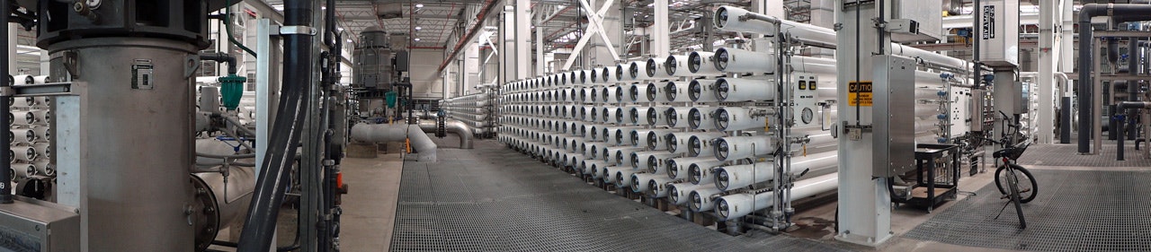 An industrial facility with rows of large cylindrical pipes, metal structures, and equipment in a spacious warehouse setting.