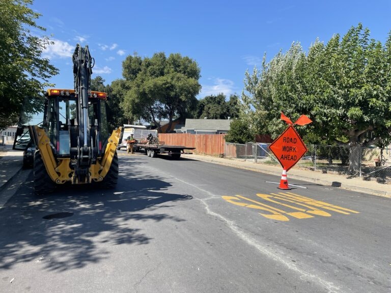 Road construction area with heavy machinery and a "ROAD WORK AHEAD" sign on a sunny day.