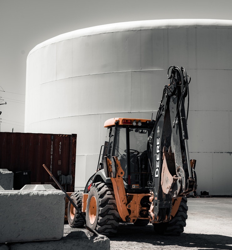 A construction vehicle on a worksite with a large cylindrical structure in the background.