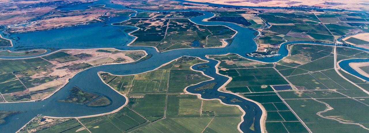 An aerial view of a river delta with various waterways surrounded by agricultural fields.