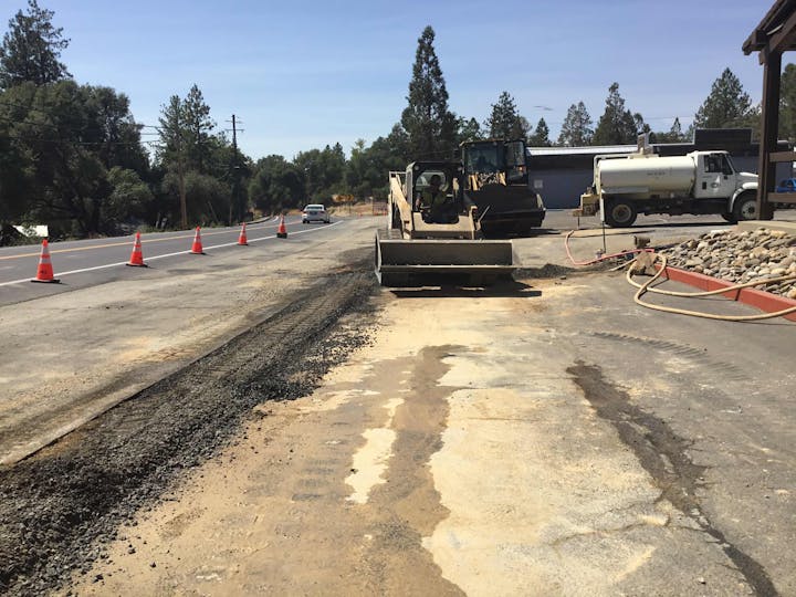 Roadwork in progress with construction equipment and traffic cones on a rural road.
