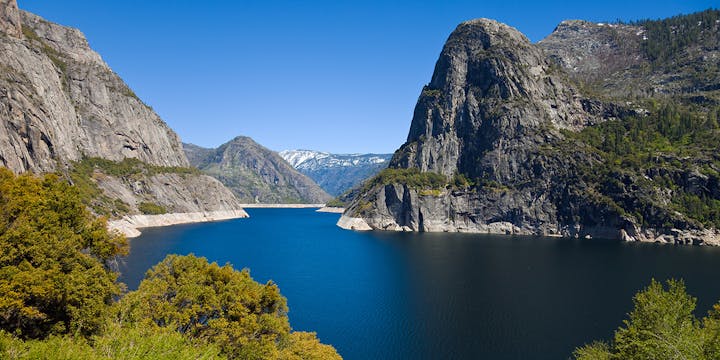 A stunning view of a mountainous landscape with a clear blue reservoir nestled between rocky cliffs under a bright blue sky.