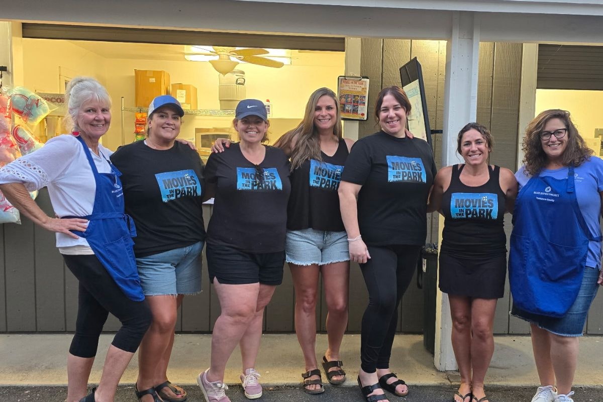 Group of women posing together, promoting "Movies in the Park," with a concession stand in the background.
