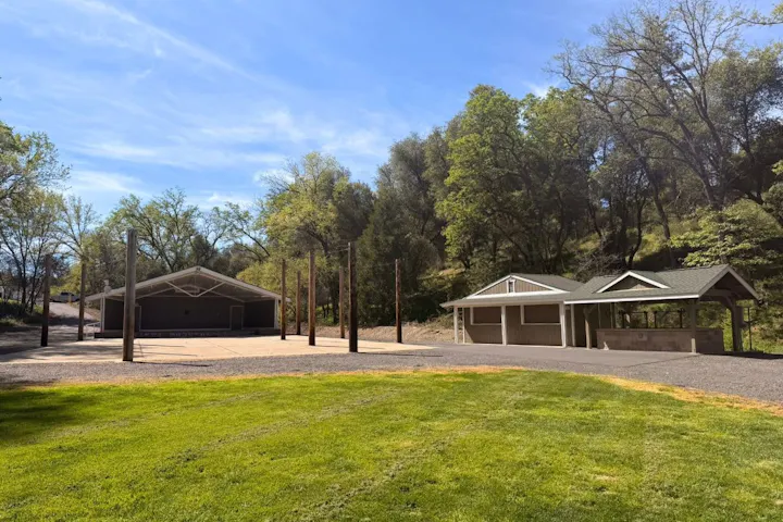 A serene outdoor area featuring two structures, a grassy space, and trees under a clear blue sky.