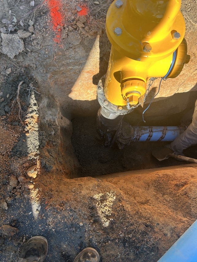 A yellow fire hydrant is being installed or repaired in an excavated hole in the ground.