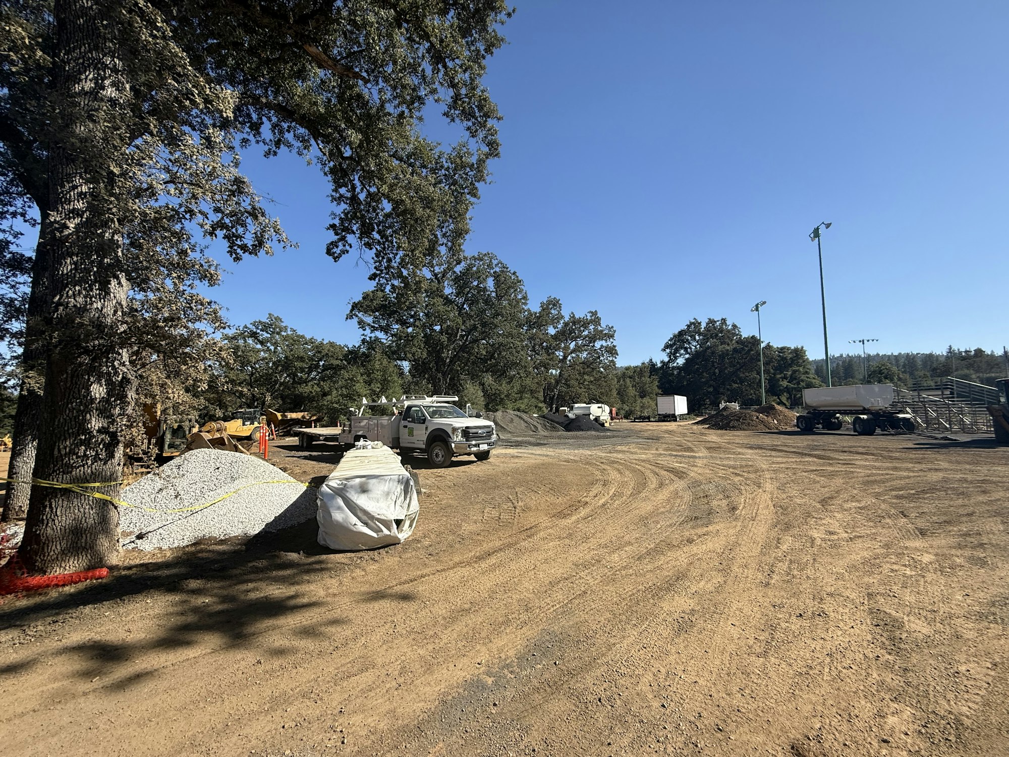 Construction site with trucks, gravel, and equipment under a clear sky.