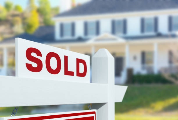 A "SOLD" sign in front of a house, indicating the property has been sold.