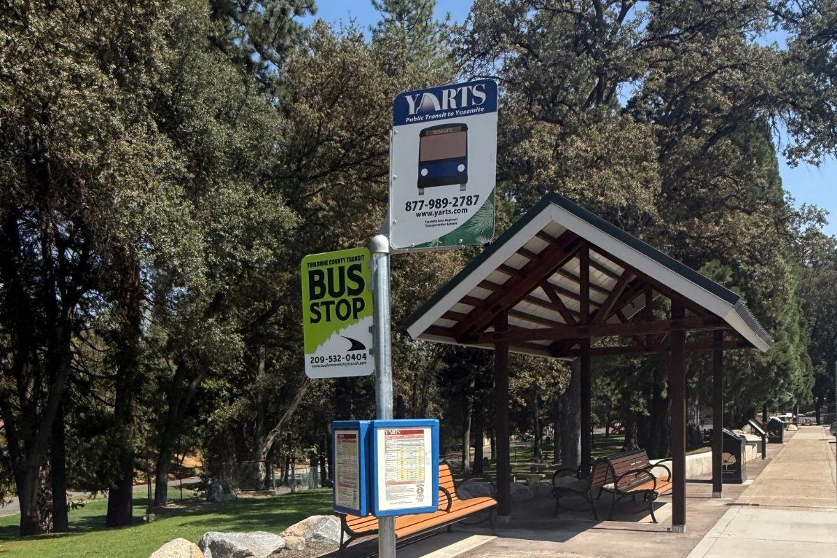 A bus stop sign for YARTS public transit to Yosemite, including a shelter and nearby seating in a park-like setting.